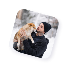 Happy man in winter clothing holding a dog outdoors in the snow
